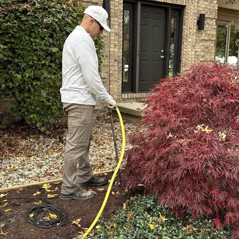 A man watering the bushes in front of his house.